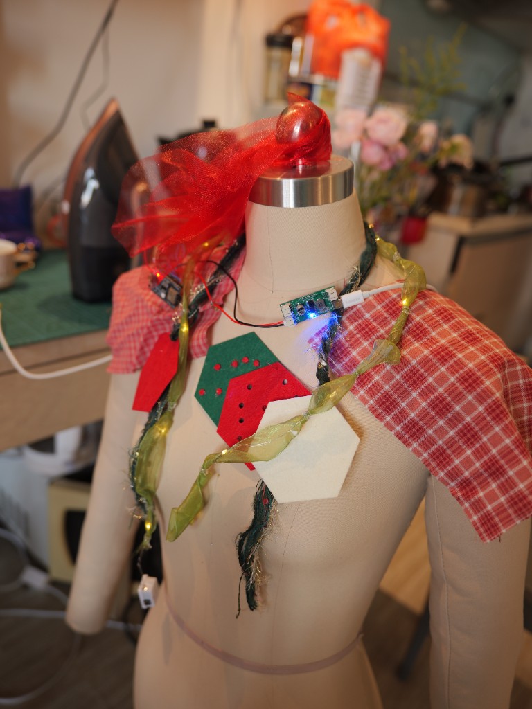 人形台架：格纹肩饰、红色薄纱、胸前毛毡六边形与颈部电路板